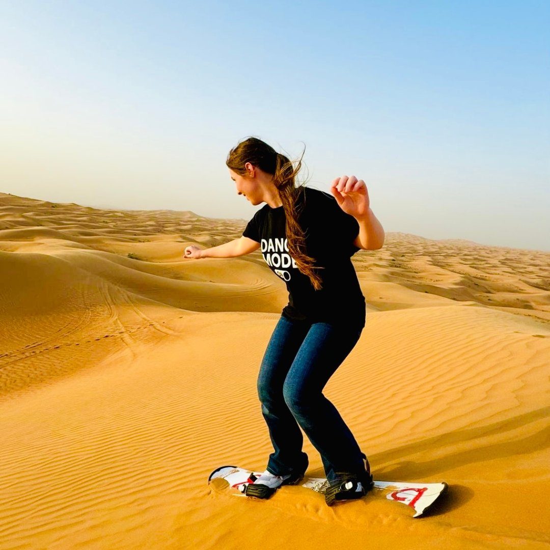 Woman sandboarding down a golden desert dune
