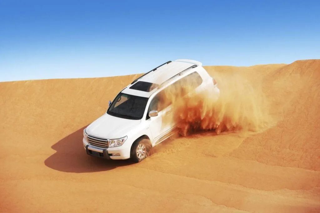 White four-wheel-drive vehicle throwing sand as it crosses a dune