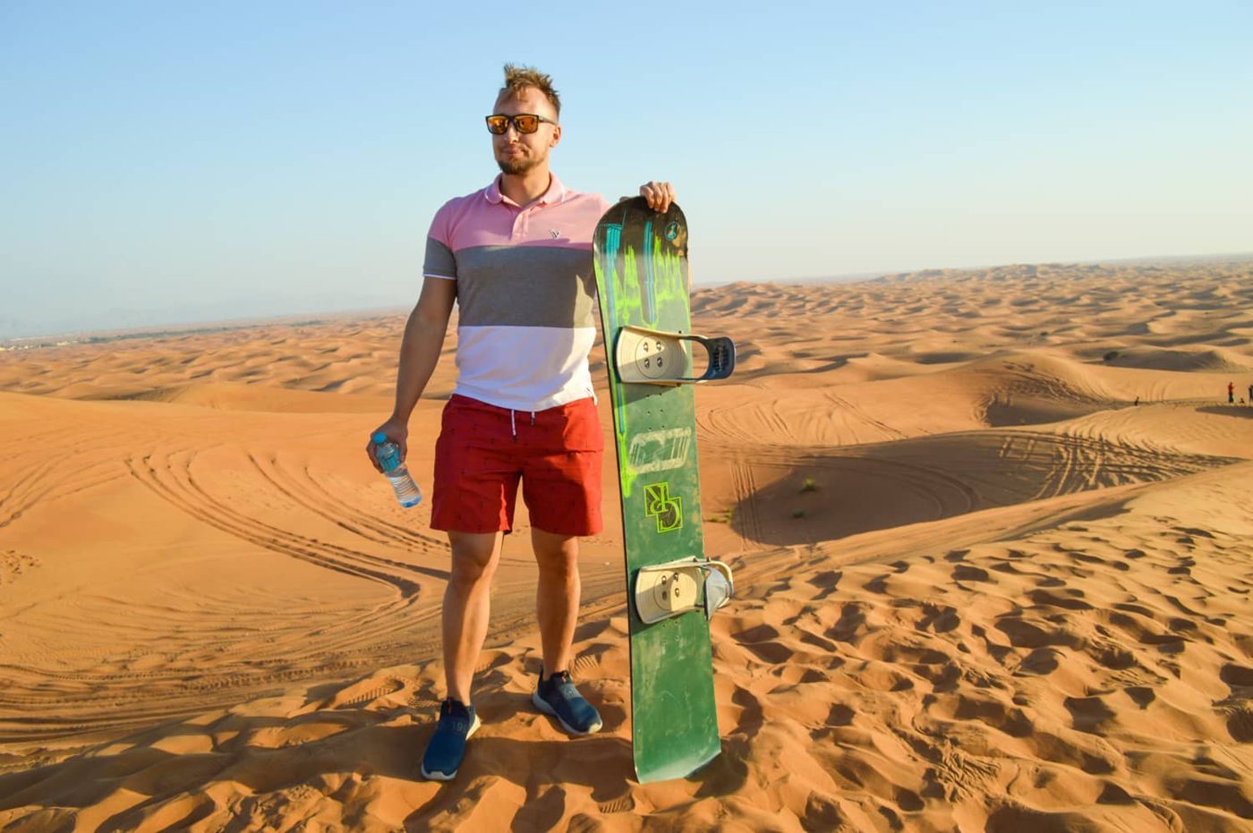 Visitor holding a green sandboard on a desert dune