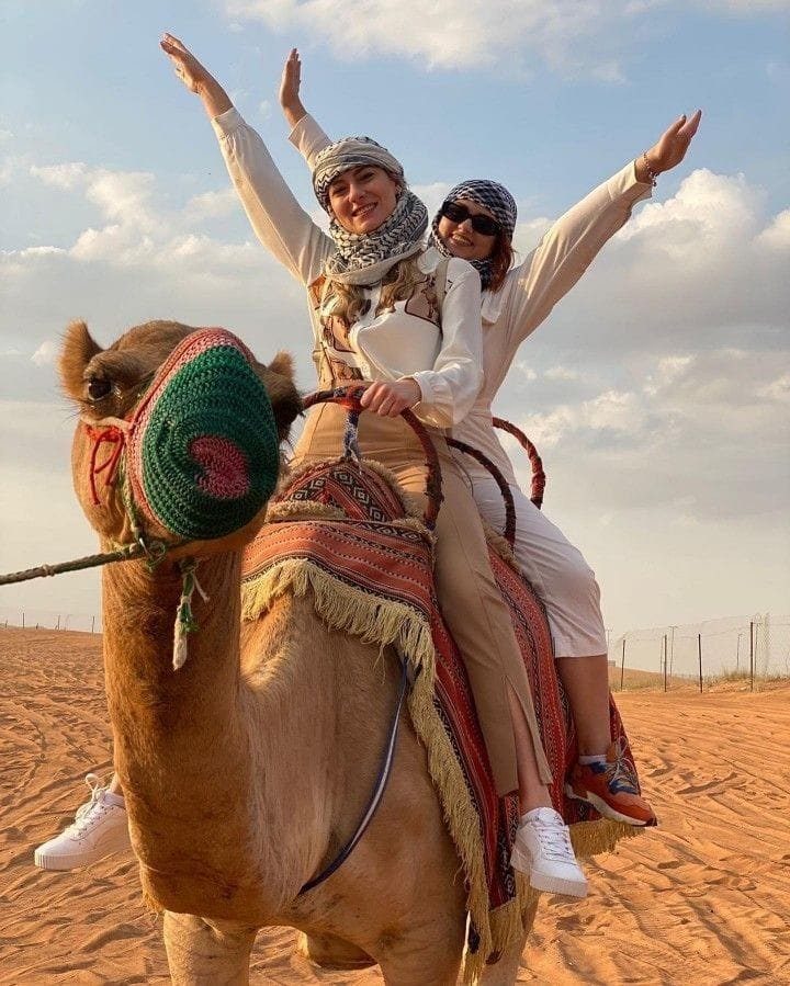 Two visitors riding a decorated camel in the desert