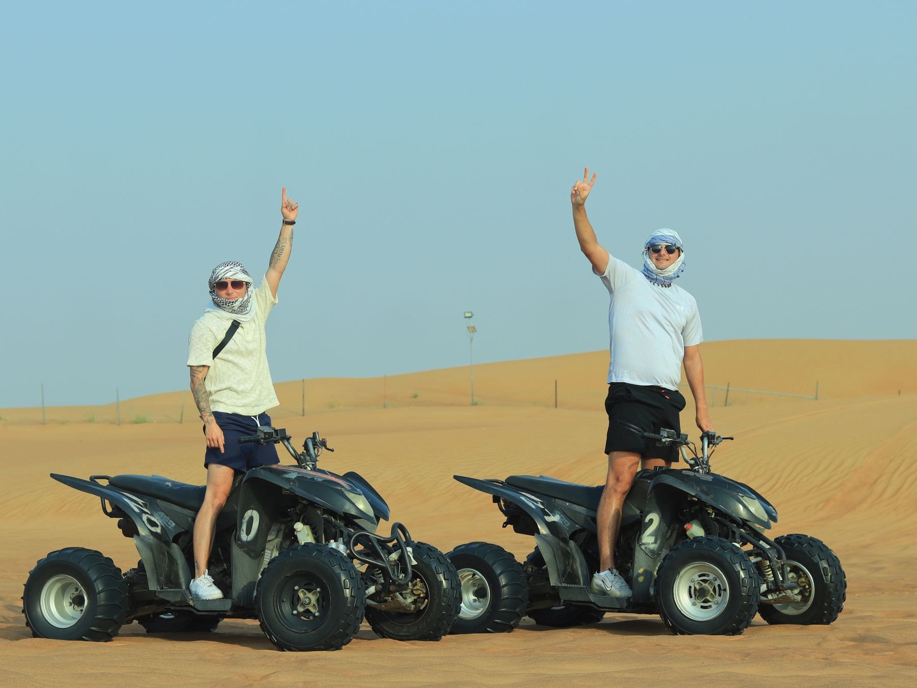 Two men standing on separate quad bikes in the Dubai desert