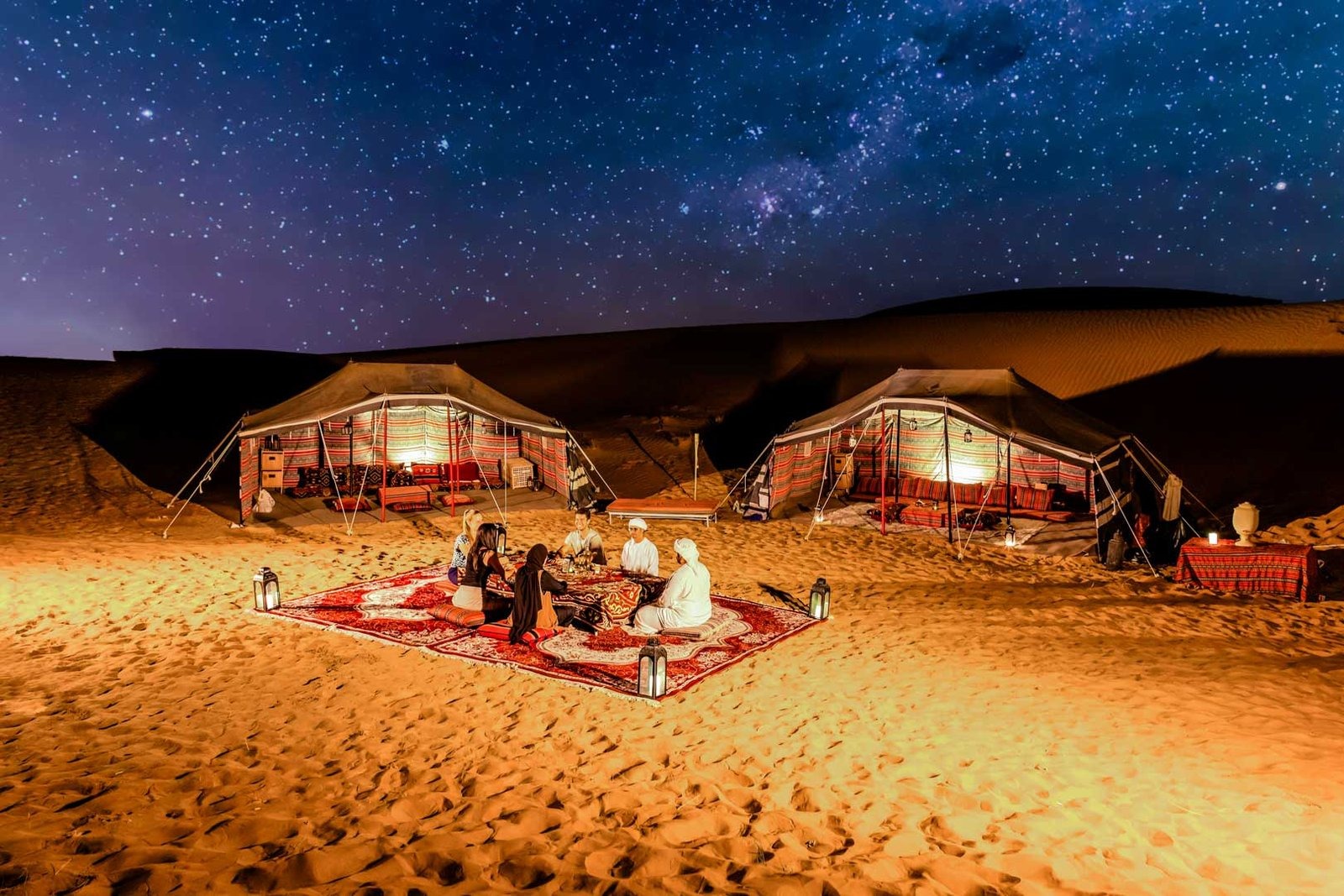 Illuminated Bedouin-style tents and a seated group beneath a starry night sky