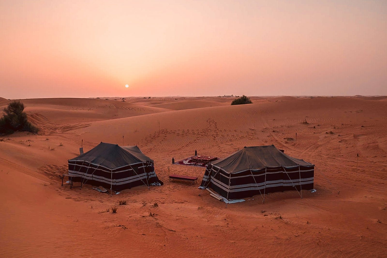 Two striped Bedouin-style tents in Dubai sand dunes at sunset